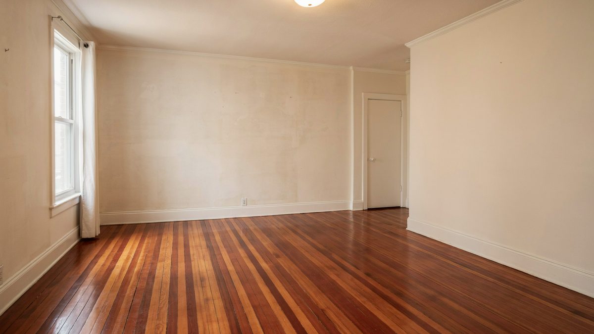 Empty room showing deep reddish mahogany boards and bare cream walls