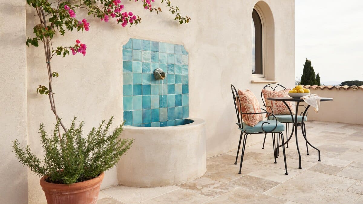 Travertine paving beside an aqua blue tiled wall fountain and teal cushioned chairs