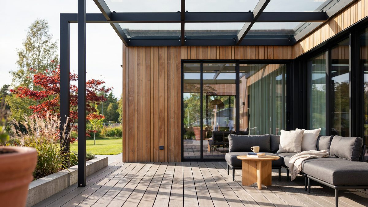 Slim black pergola with clear roof panels beside cedar clad glass doors