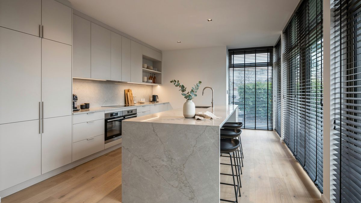 White cabinets, marble island and blinds filtering light across pale flooring