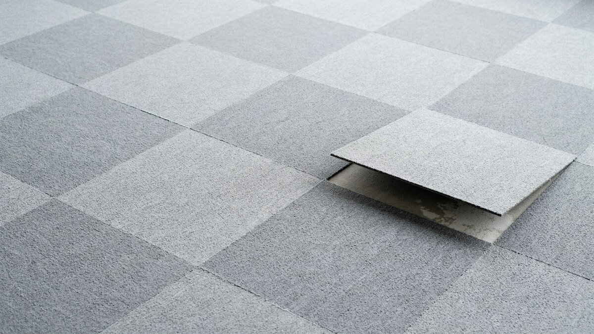 Gray olefin interlocking carpet tiles with one square lifted at the edge