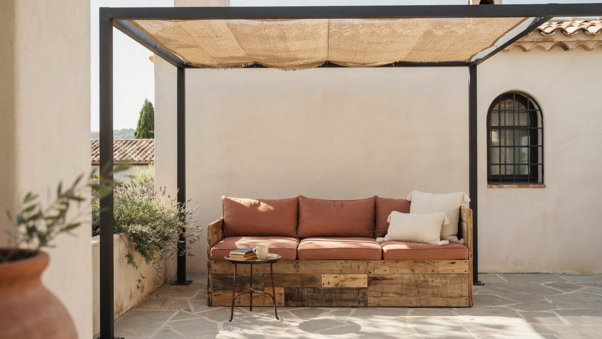 Black framed pergola with woven screen canopy above a rustic wood sofa