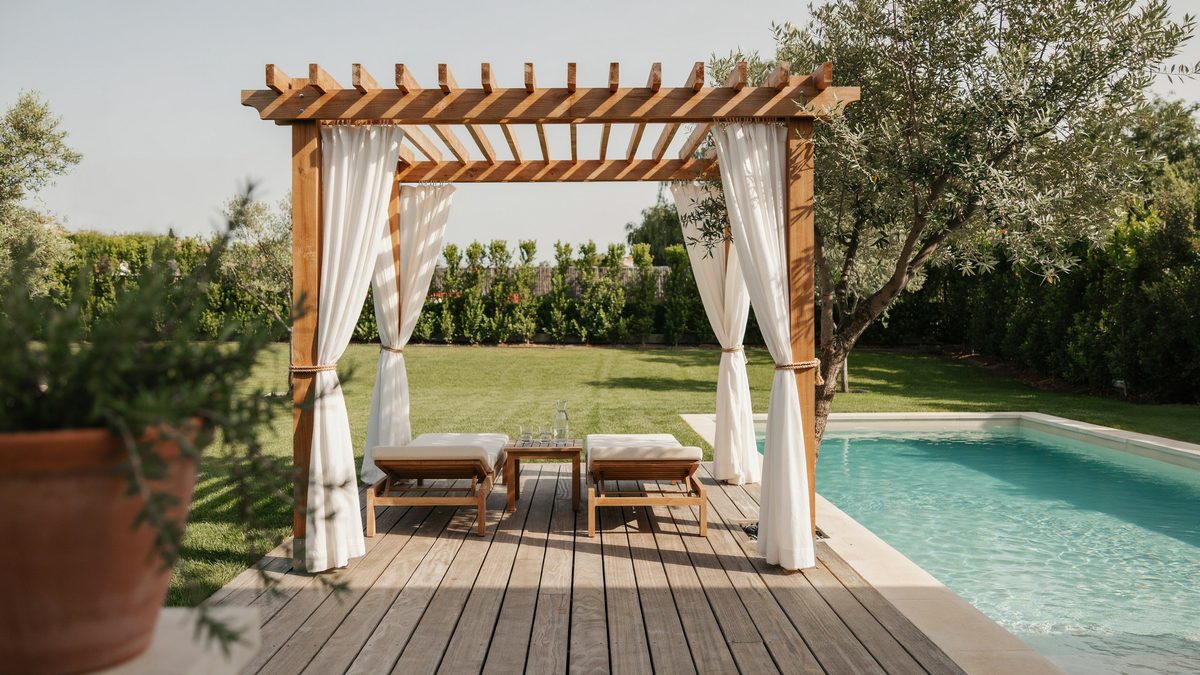 Cedar poolside pergola with white curtains and a low daybed platform