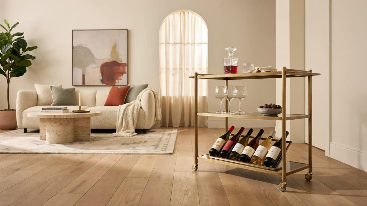 Portable brass bar cart with a lower wine rack beside a cream sofa in a bright living room