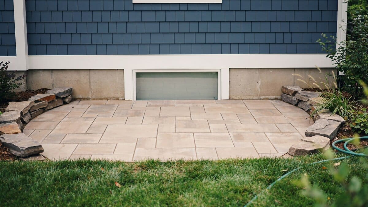 Raised sandstone paver landing with a rock border against navy blue siding