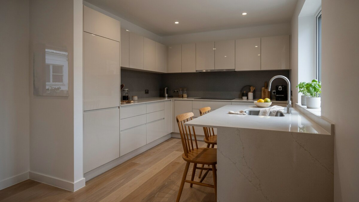 Glossy white cabinets meet a quartz peninsula with wood chairs in a compact footprint