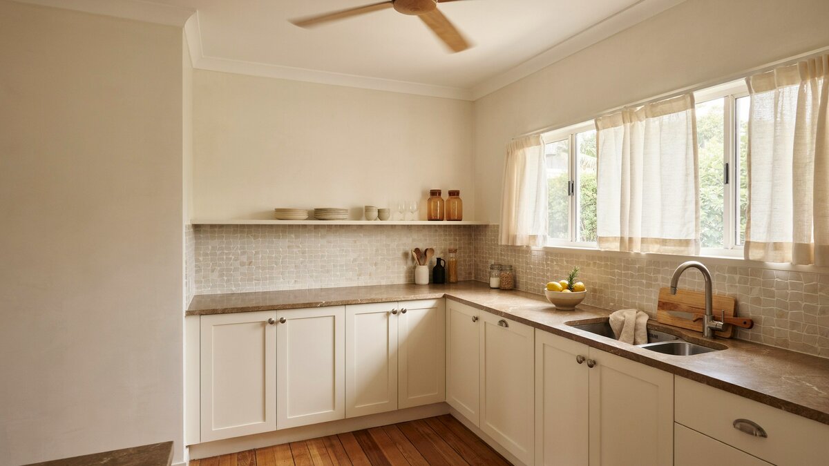 Sliding windows and a ceiling fan above cream recessed panel cabinets and a corner sink