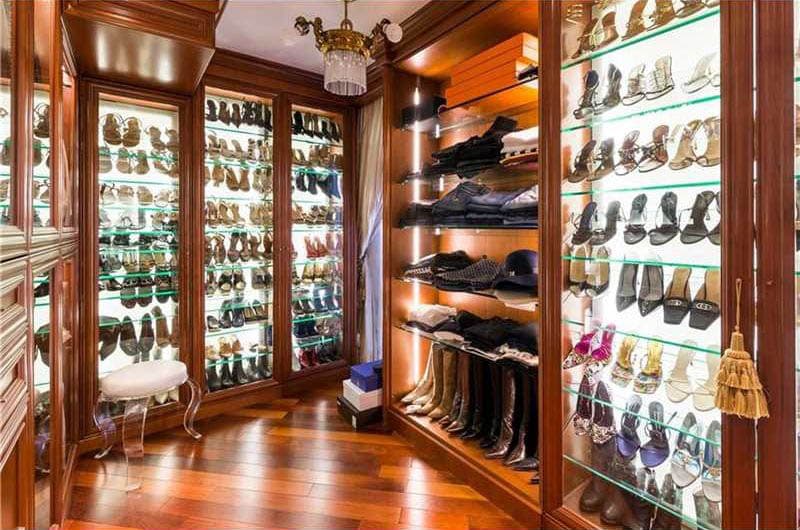 Expansive closet with lighted wood cabinet glass doors, glass shelves for shoes and chandelier
