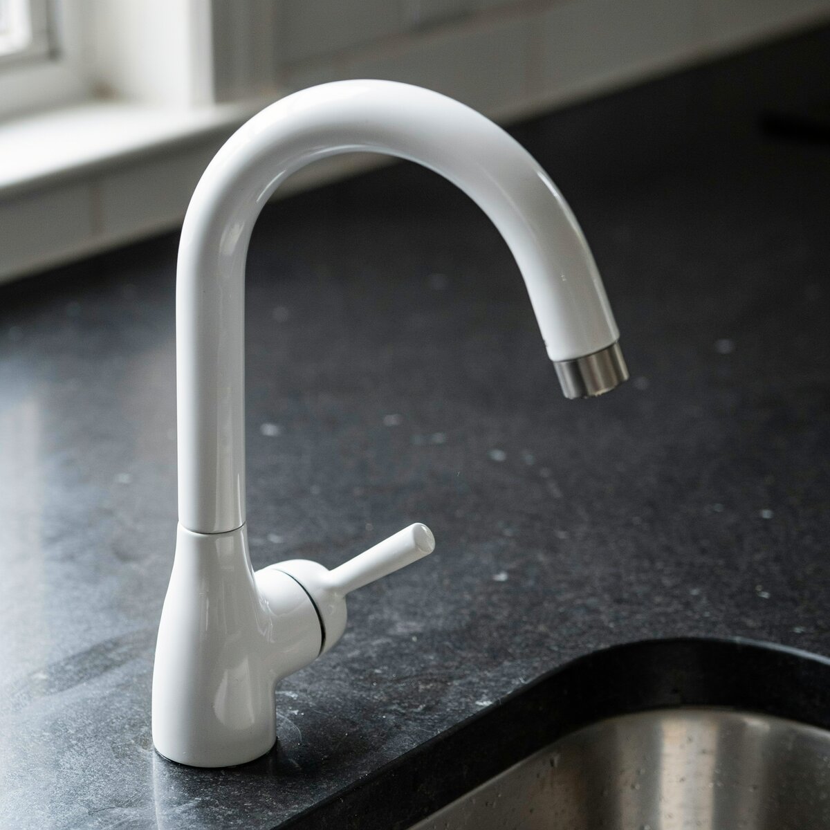 White gooseneck faucet with single handle against dark countertop
