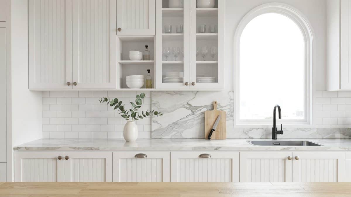 White beadboard drawer fronts beneath a marble counter and a tall arched window