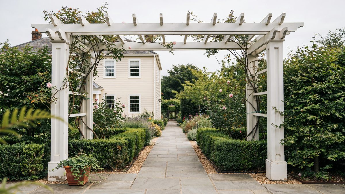 White garden arbor pergola with creeping vines above a stone walkway