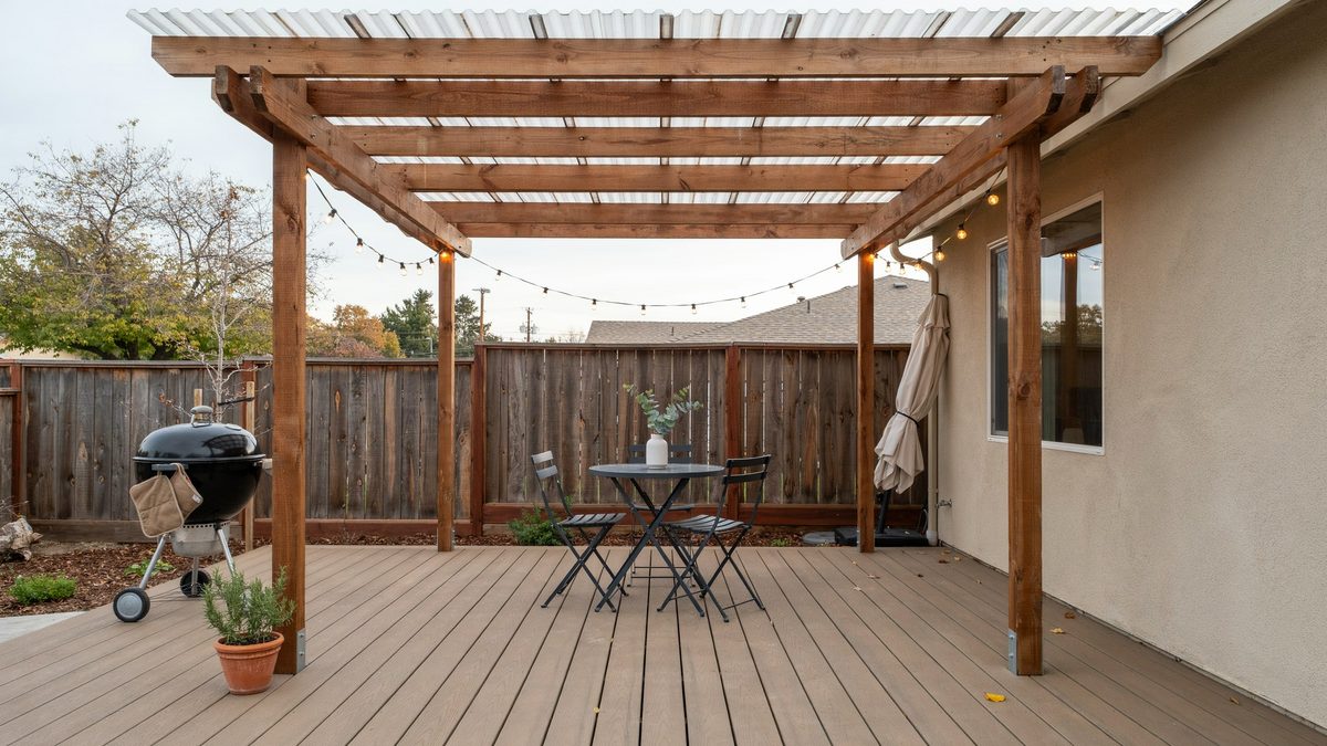 Corrugated roof pergola over a small deck with a grill and bistro set