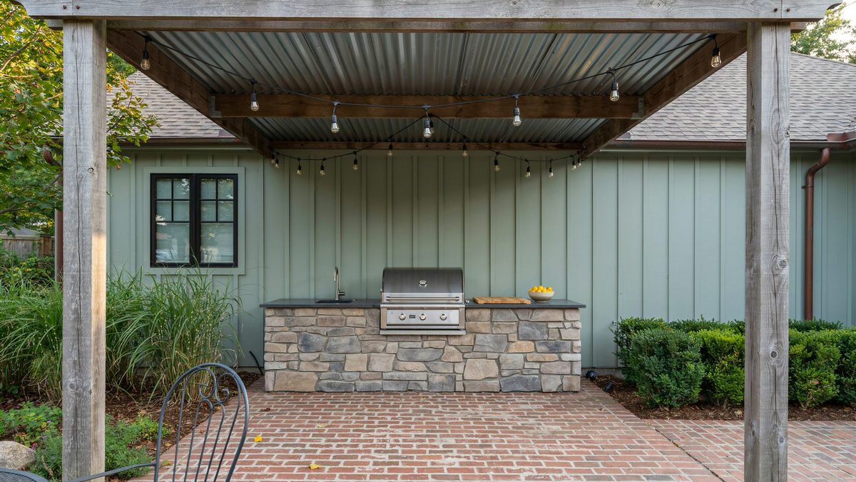Metal roofed pergola with string lights above a brick patio outdoor kitchen