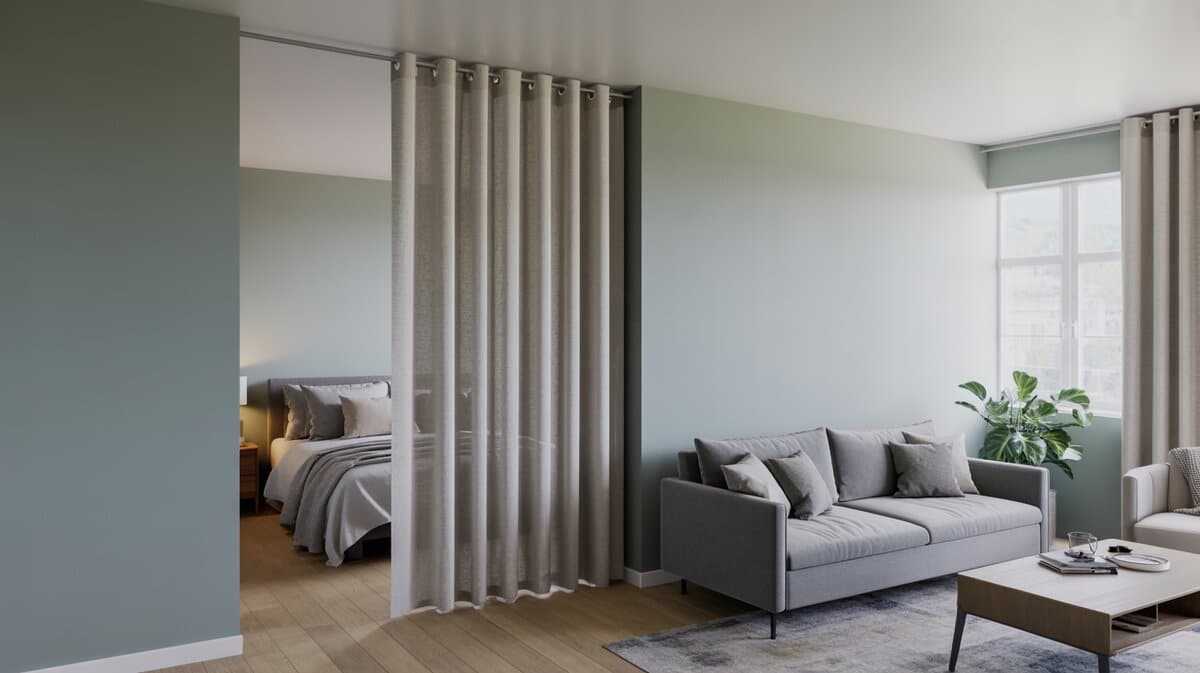 Sage green studio with curtain dividing gray sofa from bed near bright window