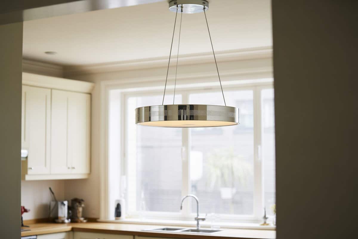 Polished chrome drum pendant on slim cables above a bright kitchen counter