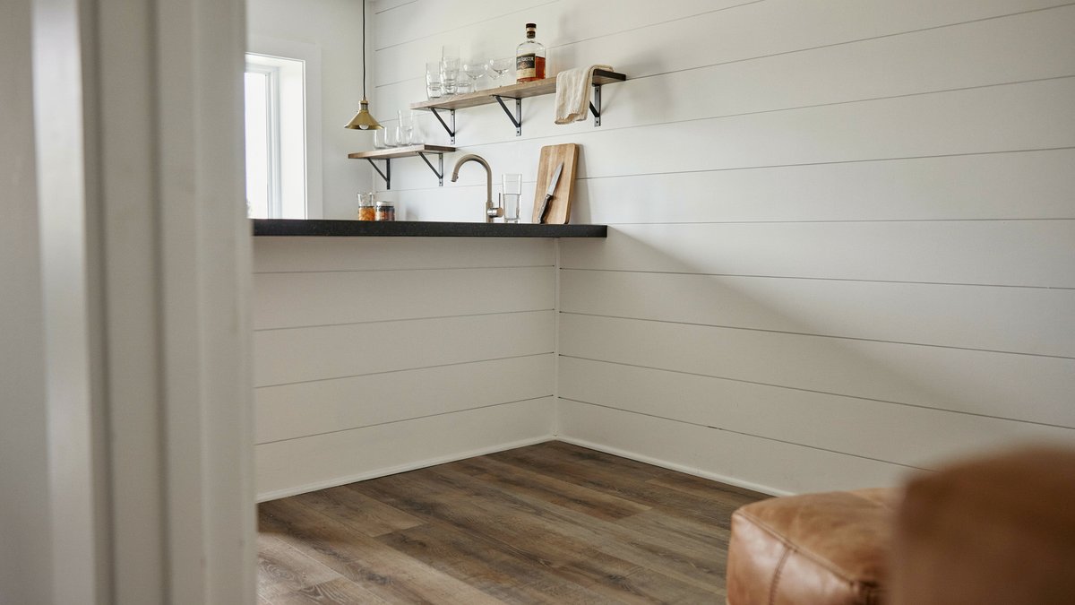 White shiplap corner bar with brass faucet over dark vinyl plank