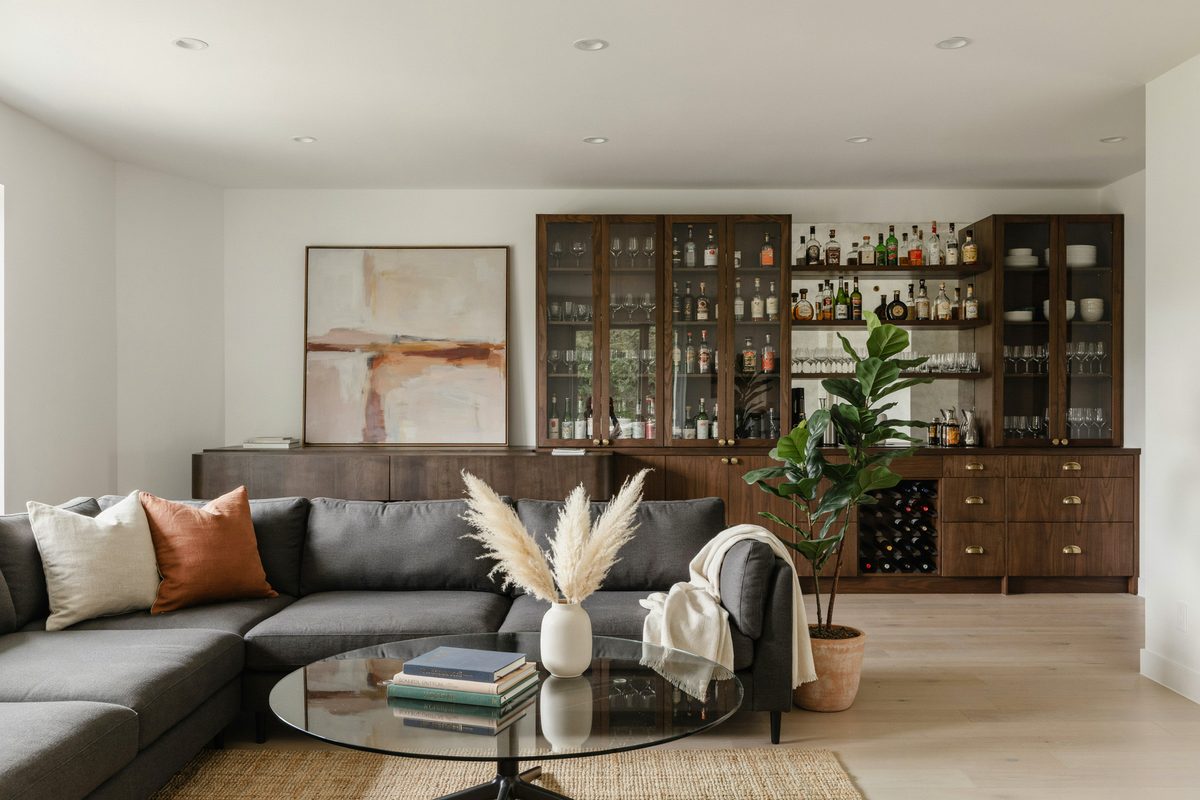 Dark wood back bar cabinetry facing a gray sectional on hardwood flooring