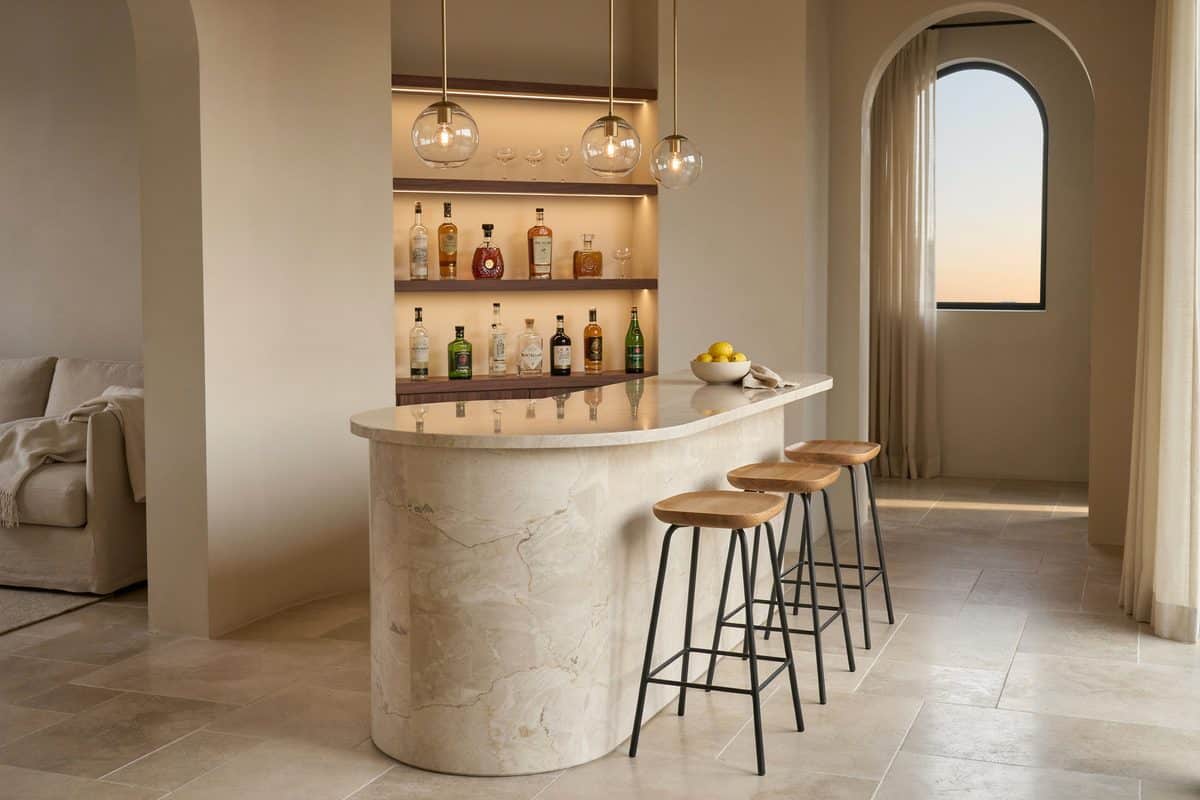Curved pale stone bar counter under glass pendants with four wood stools