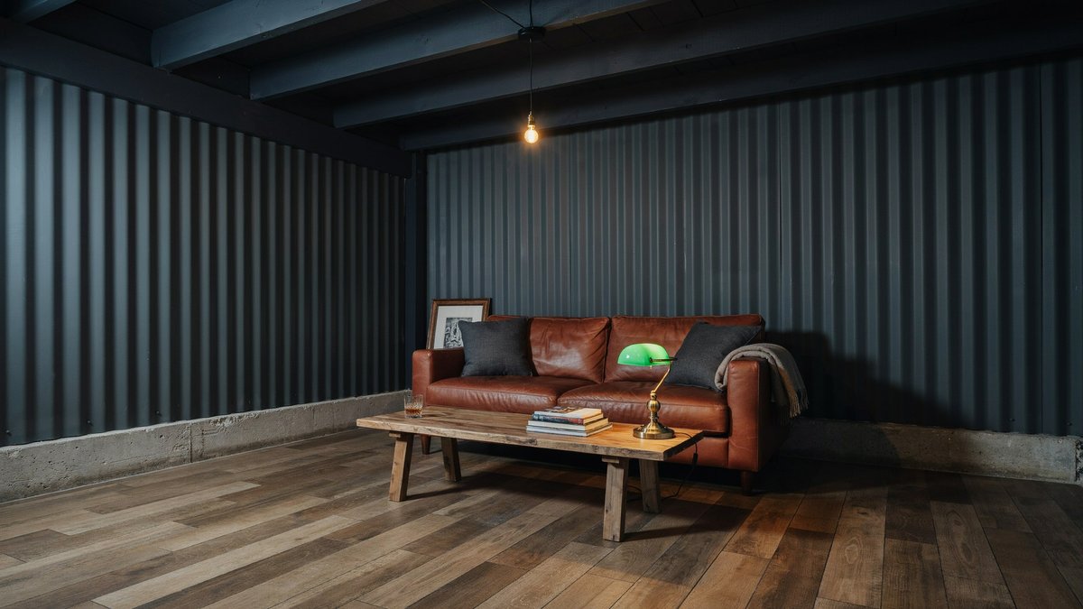 Hickory vinyl planks beneath a leather sofa and charcoal corrugated steel wall