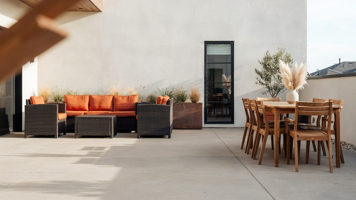 Rattan patio sofa set with bright orange cushions beside a teak dining table