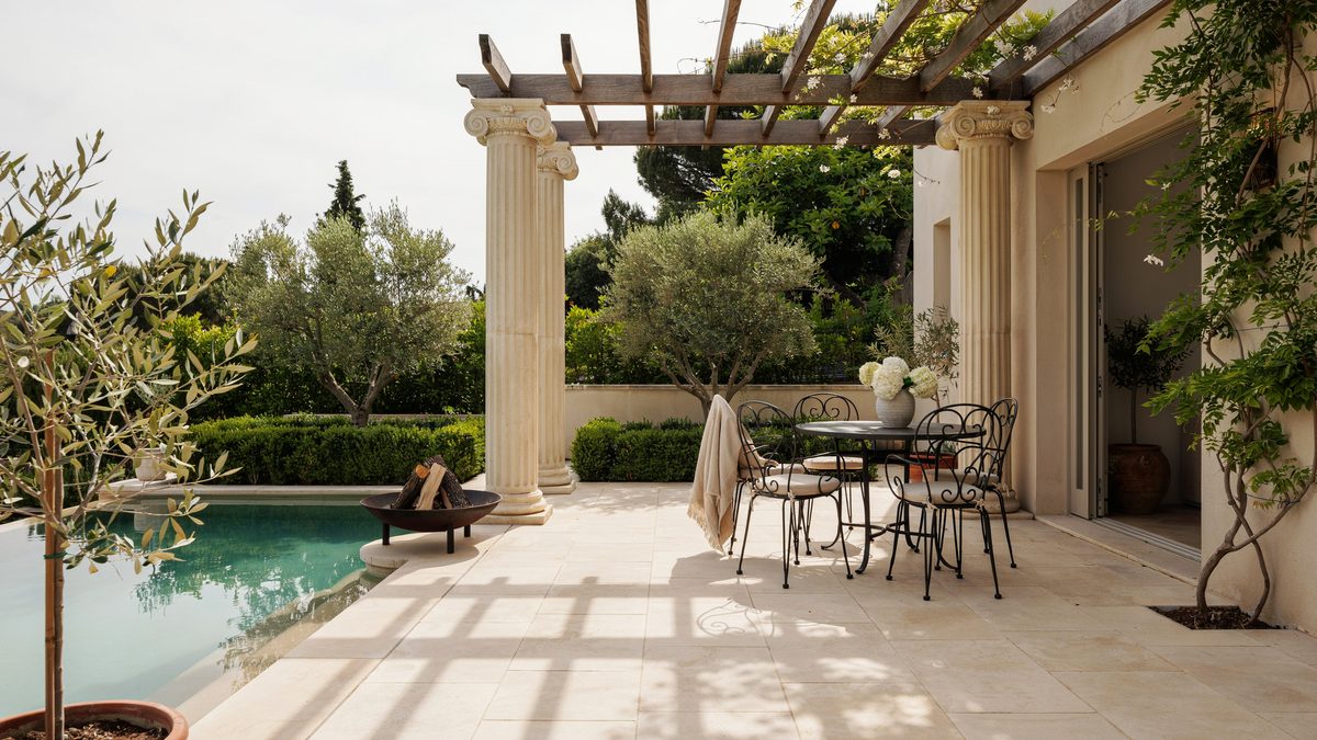 Sandstone tiled patio with ionic columns, teak trellis and black iron furniture