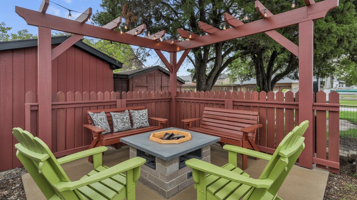 Rustic red wood corner pergola with lime green Adirondack chairs around square concrete block fire pit