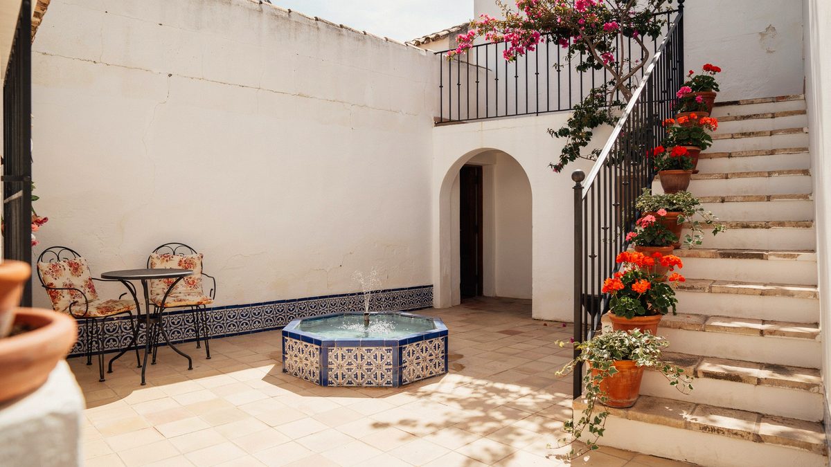 Spanish courtyard with tiled fountain, wrought iron chairs and potted geraniums
