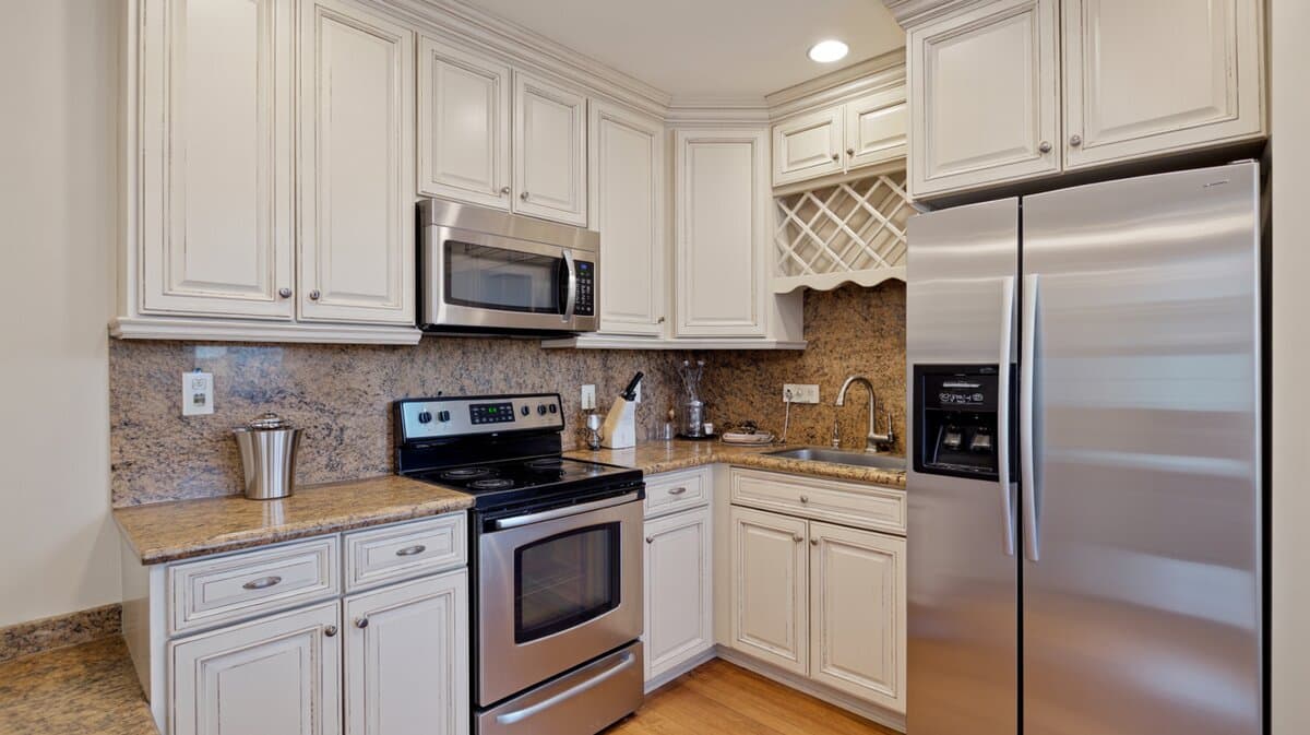Compact traditional white distressed kitchen with speckled brown granite countertops, electric range and side-by-side refrigerator