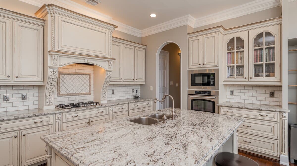 Ornate antique white raised-panel kitchen with granite island, arched range hood, subway tile backsplash and stainless ovens