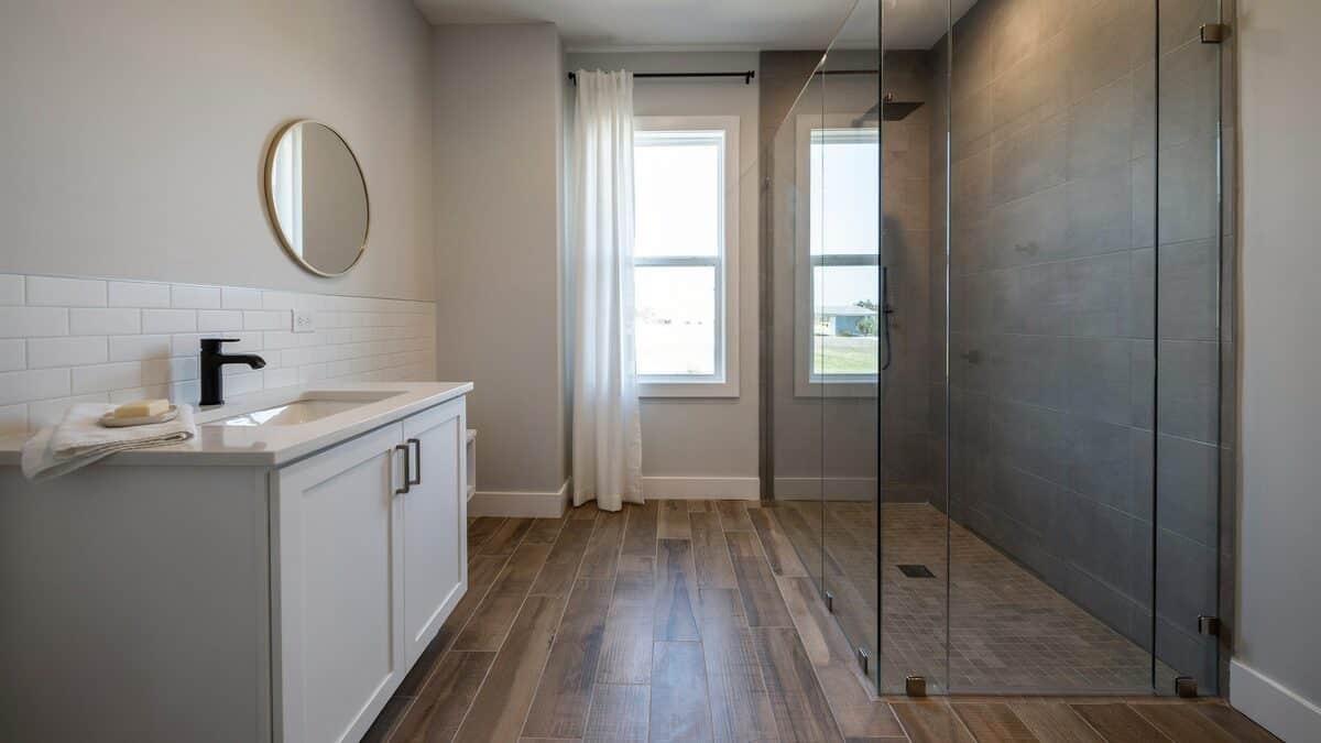 Wood look vinyl planks running past a white vanity toward a glass shower
