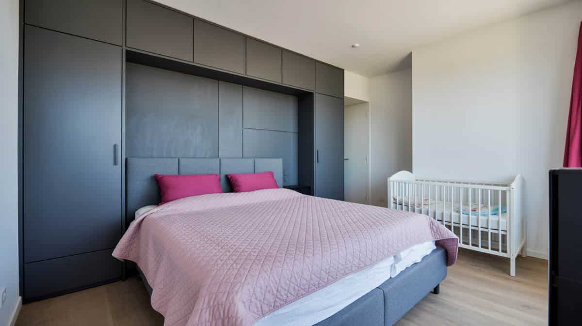 Apartment bedroom with matte black paneled side wall, gray platform bed, pink quilt, and white crib