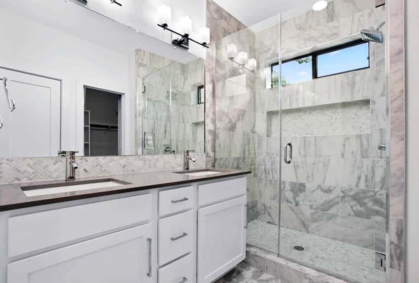 Bathroom with marble shower flooring and white vanity with marble backsplash
