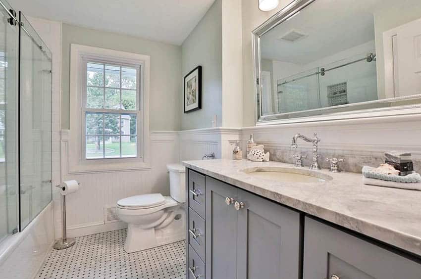 Bathroom with white wainscoting basketweave floor tile and marble counter vanity