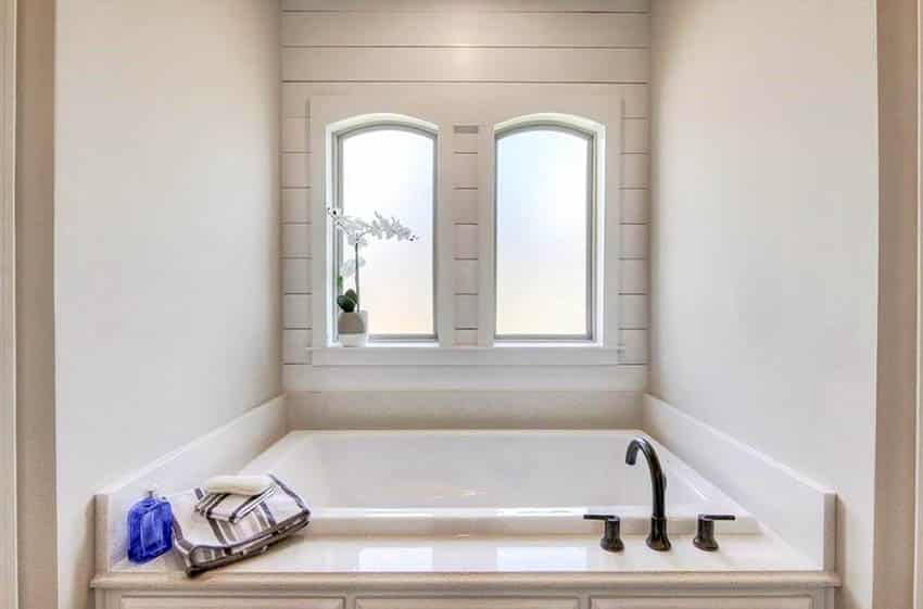 Bathtub with shiplap accent wall and arched windows