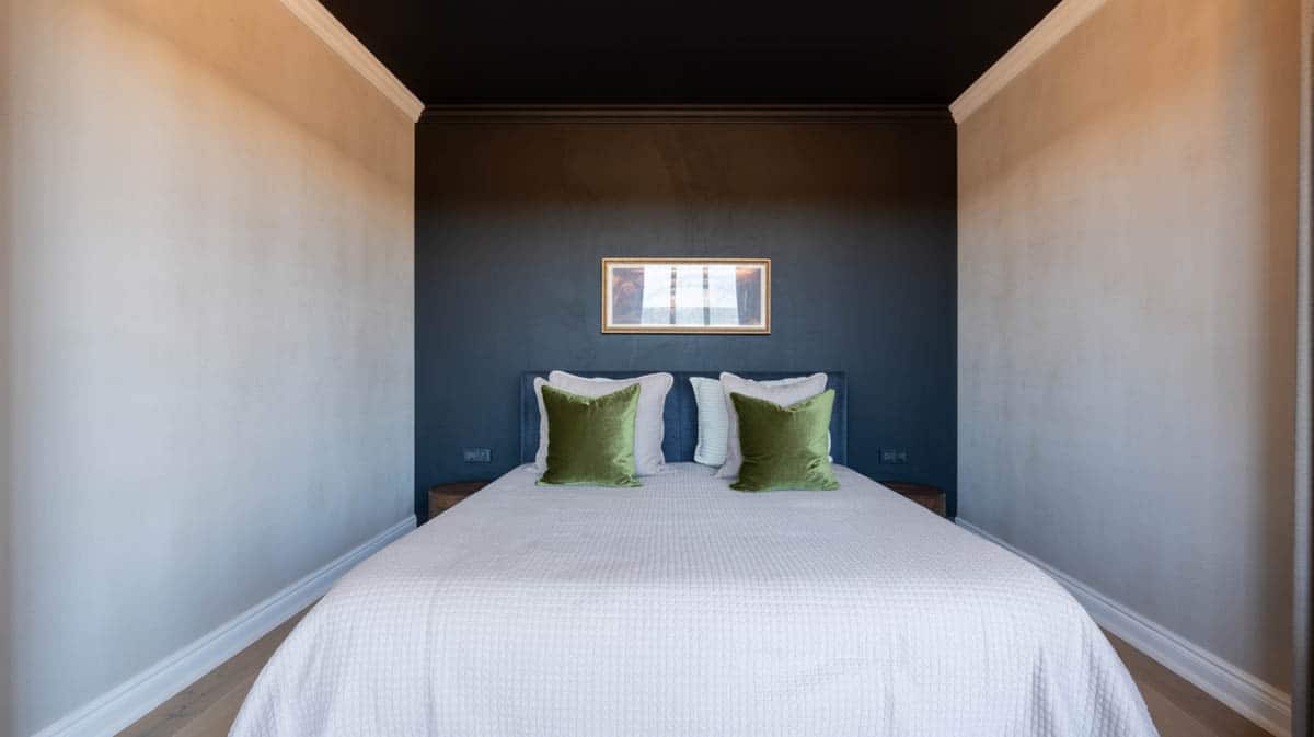 Bedroom with deep black navy accent wall, green velvet pillows, and rectangular wall art