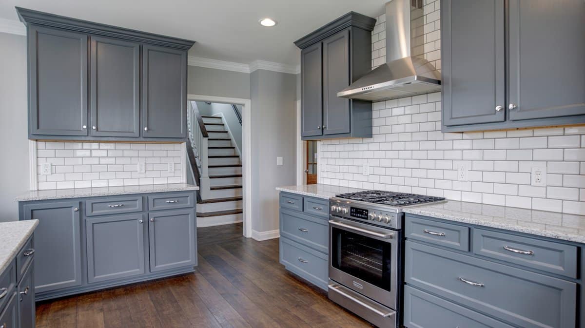 Medium-gray raised-panel cabinets with white subway tile backsplash, stainless range, and dark hardwood floors.