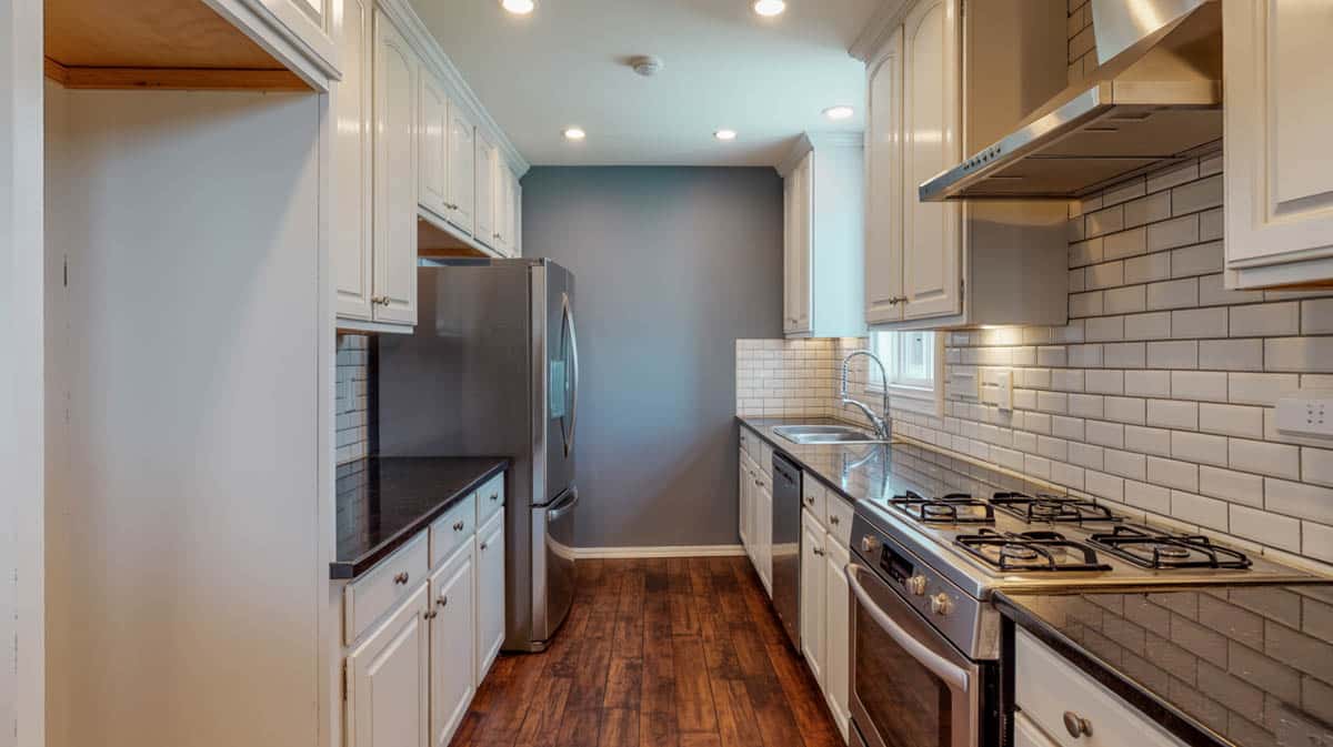 Narrow galley kitchen with gray accent wall, white brick subway tile backsplash, and black granite countertops
