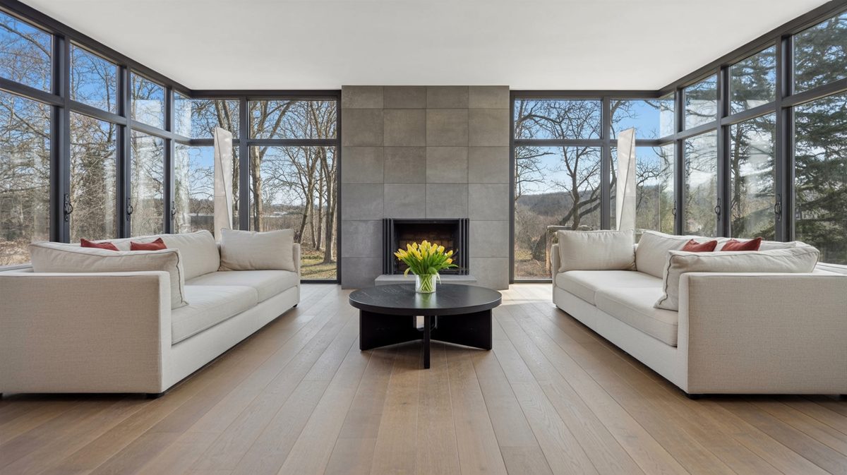 Sunlit living room with floor-to-ceiling glass curtain walls, gray tile fireplace, and yellow tulips