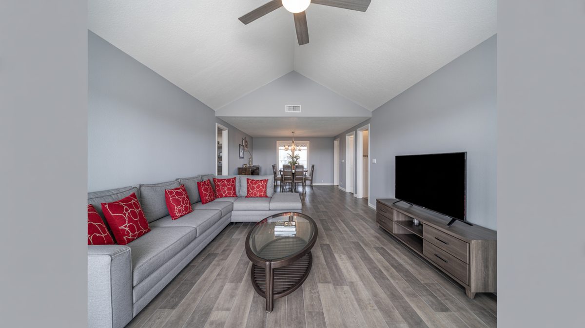 Open-plan gray living room with vaulted ceiling fan, sectional sofa, and bright red accent pillows