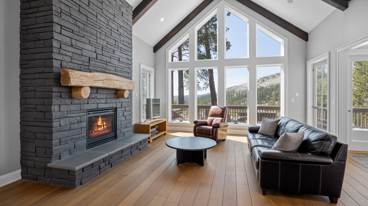 Vaulted living room with dark stacked stone fireplace, raw log beam mantel, and mountain views