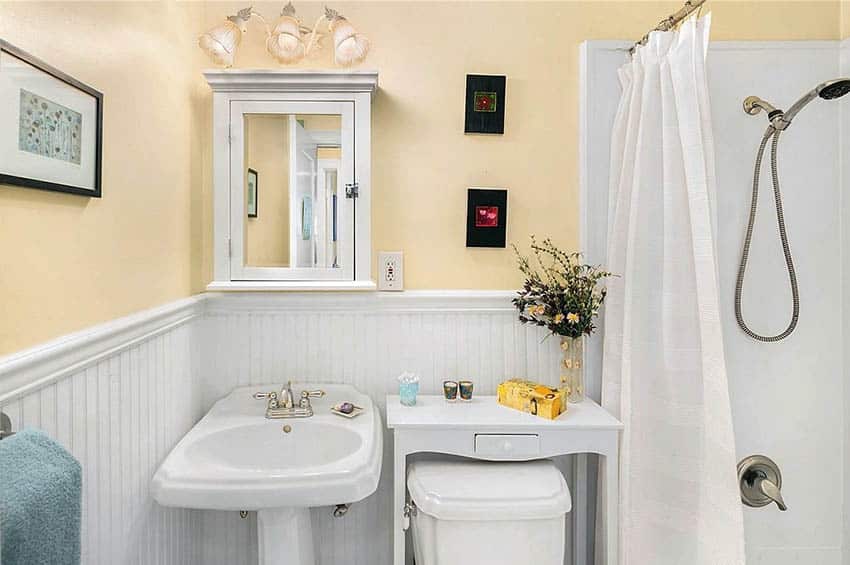 Guest bathroom with board wainscoting panels, yellow walls and pedestal sink