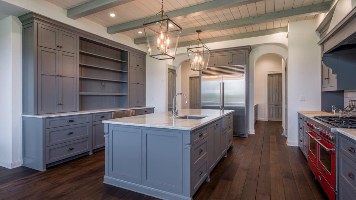 Periwinkle-gray inset cabinets with brass lantern chandeliers, a white marble island, red range, and open shelving wall.