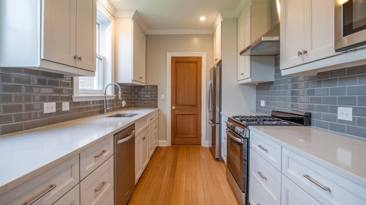 Modern galley kitchen with white shaker cabinets gray subway tile backsplash and natural wood door