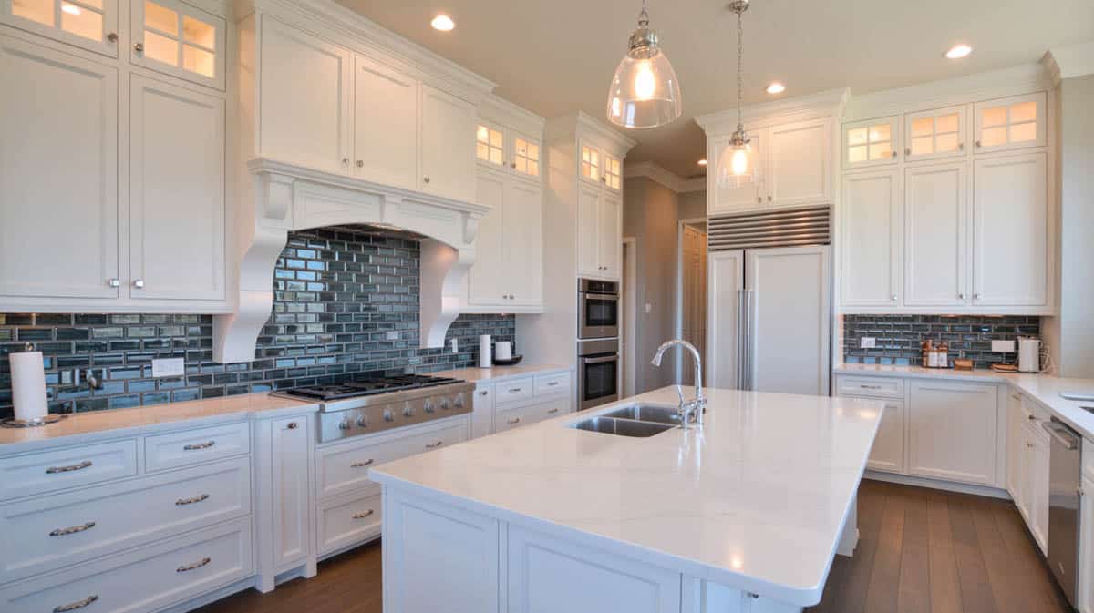 Bright all-white kitchen with dramatic black glass tile backsplash and large waterfall island
