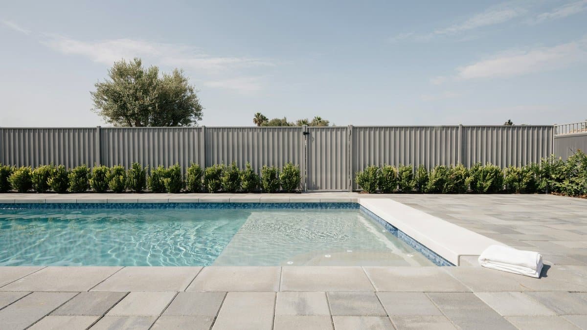 Gray aluminum safety fence beyond a tiled swimming pool with bench seating