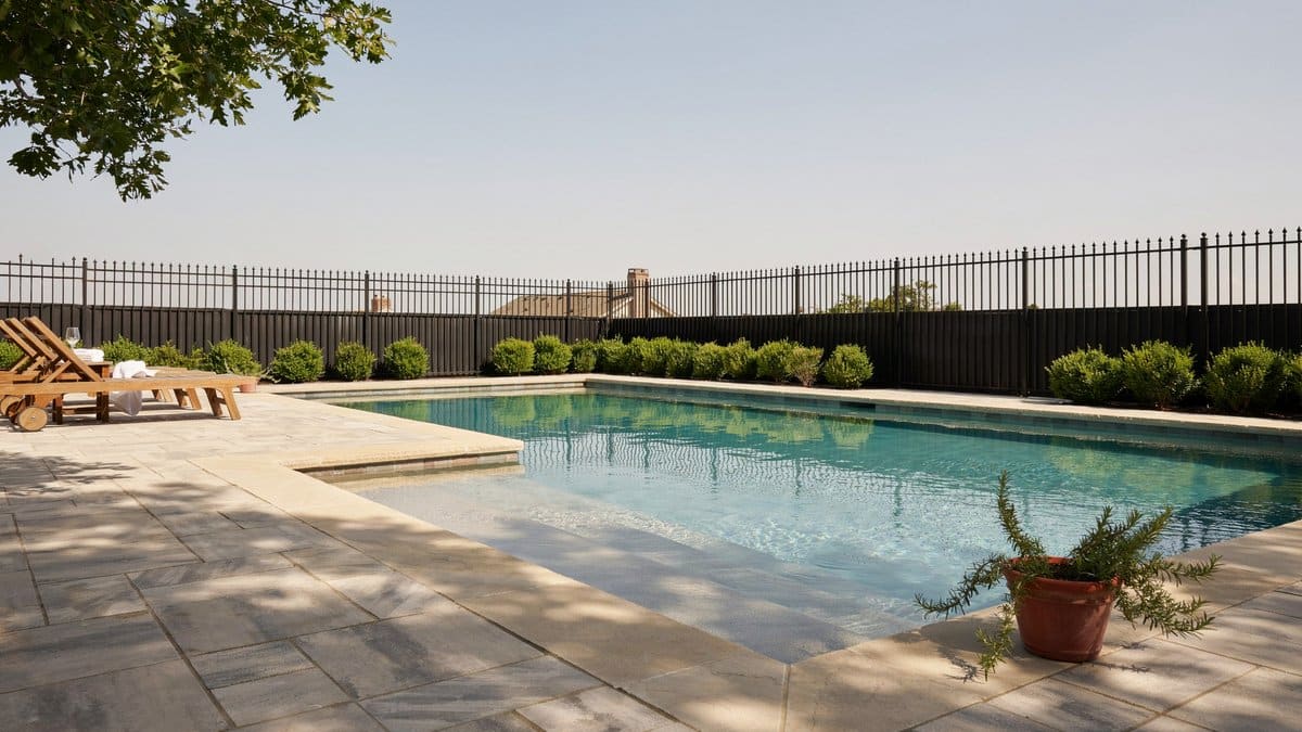 Dark metal fence with vertical bars around a paved swimming pool