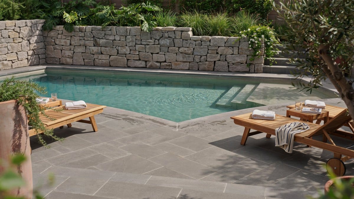Stacked stone privacy wall with wood bench framing a backyard pool