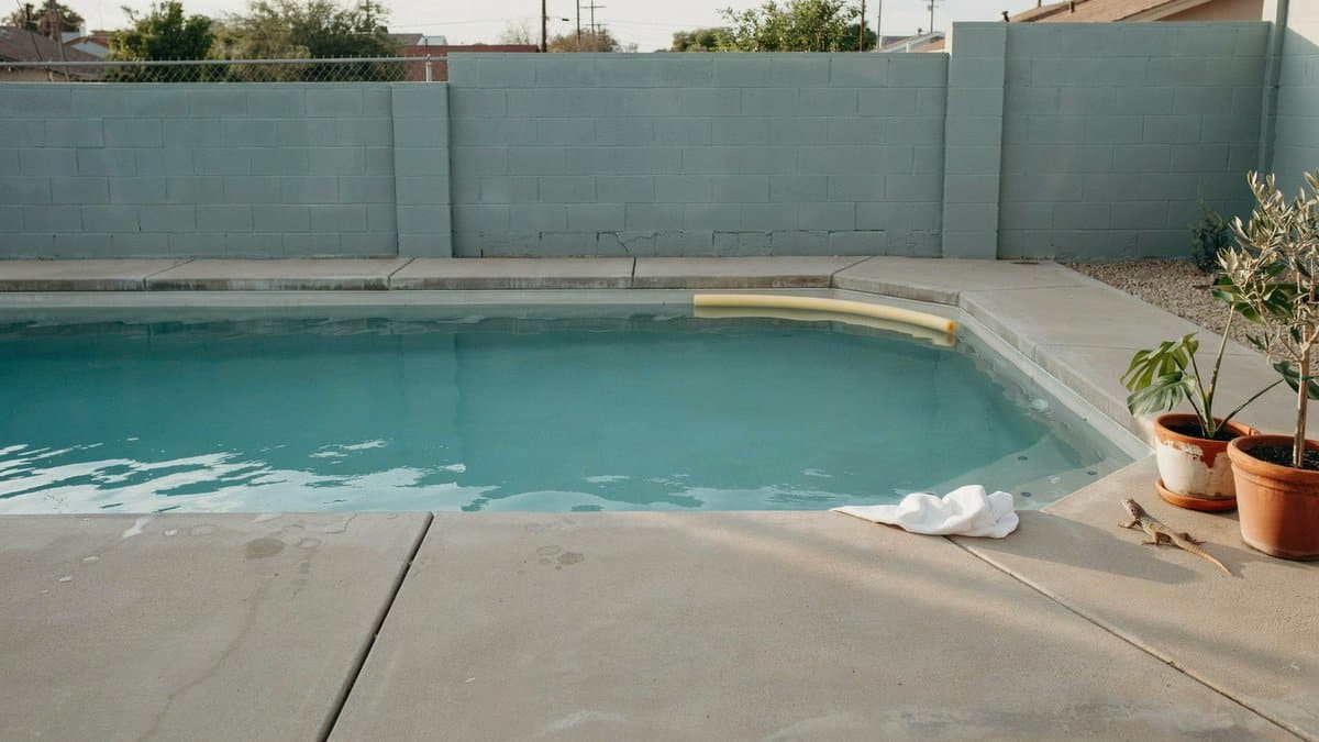 Painted cinder block wall enclosing a simple concrete backyard pool deck