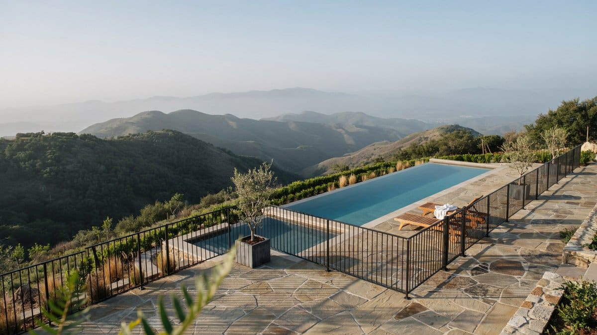 Terraced hillside infinity pool with black aluminum fence against a mountain backdrop