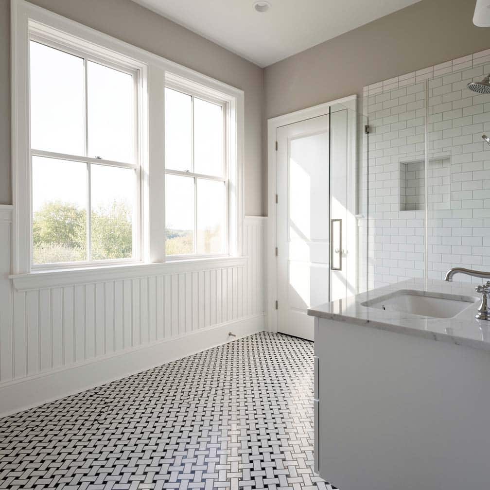 White beadboard panels below large windows with basketweave mosaic floor tile and subway tile shower